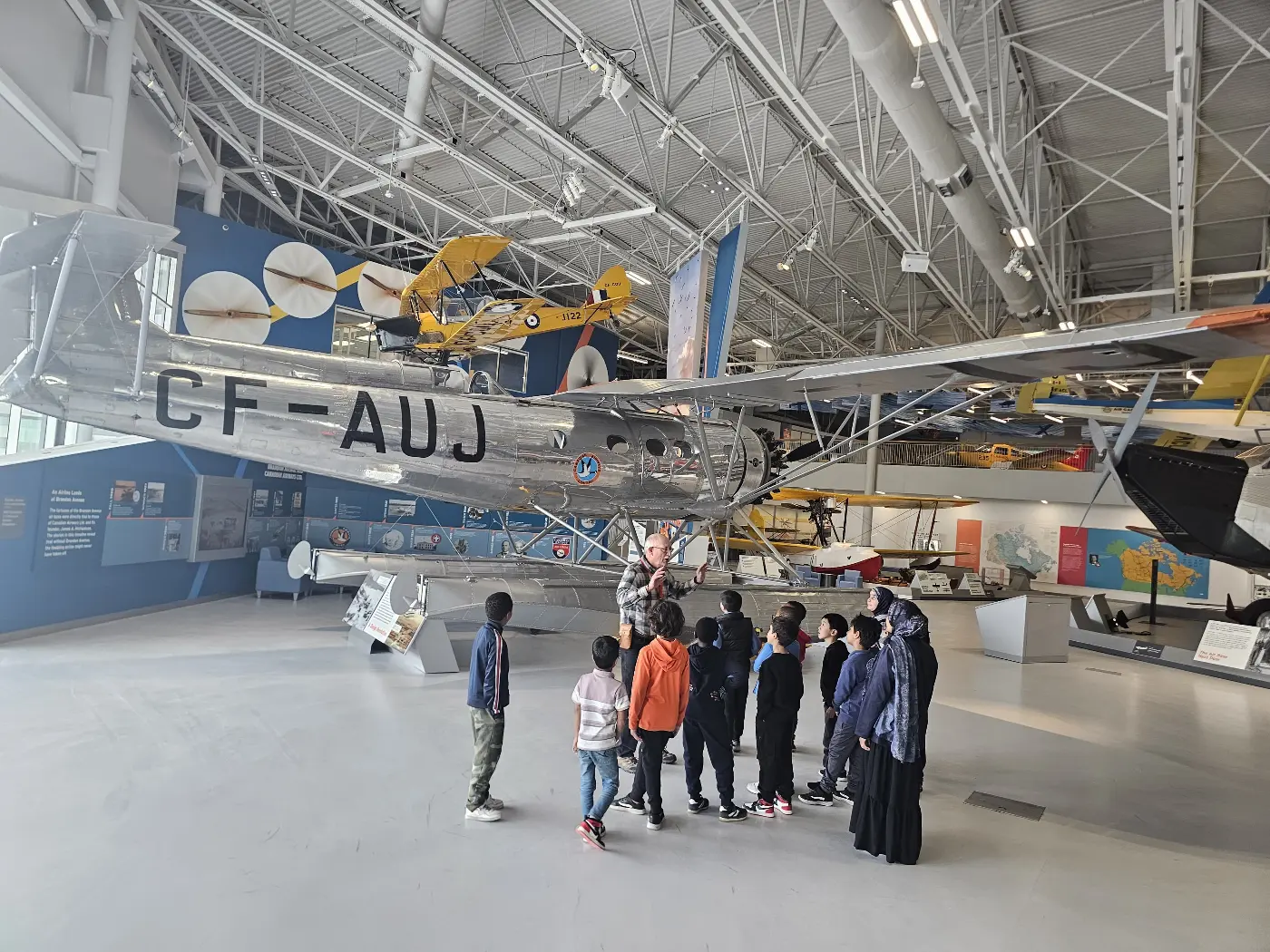 Students on a guided tour beneath a vintage aircraft at the Royal Aviation Museum of Western Canada